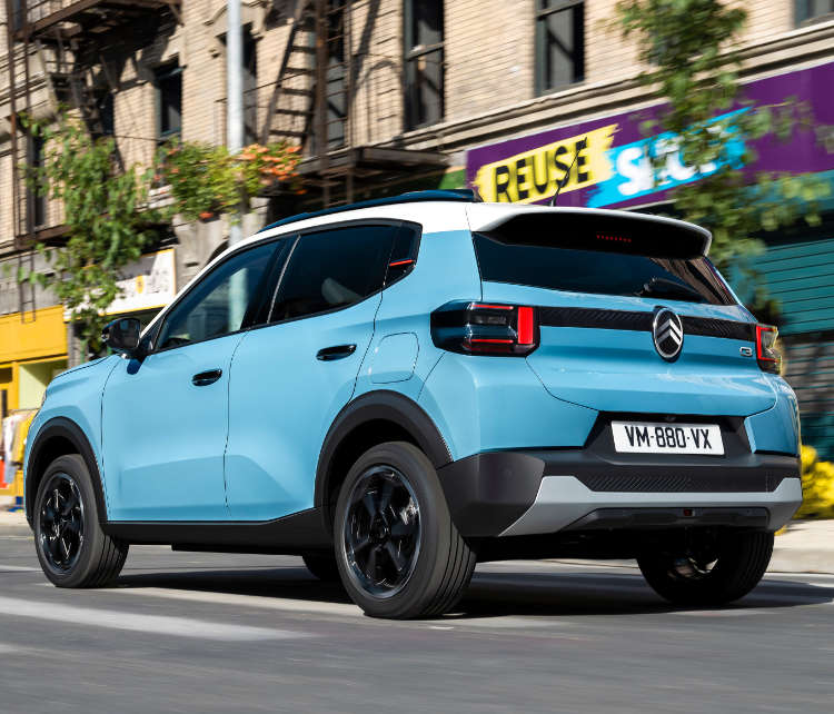 Citroën C3 блакитного кольору їде по вулиці, вигляд ззаду з лівого боку